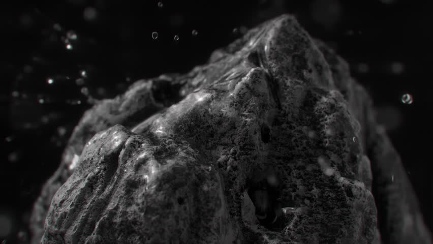 Water droplets falling on a rock surface close up. Aqua drops falls and splashing on a stone. Concept of natural springs and wellness or beauty products. Cold mineral water in super slow motion