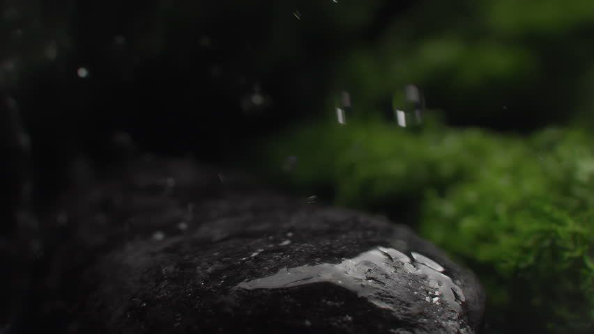 Water droplets falling on a rock surface close up. Aqua drops falls and splashing on a stone. Concept of natural springs and wellness or beauty products. Cold mineral water in super slow motion