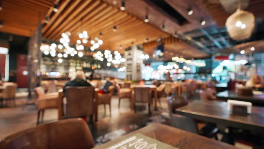Blurred interior of large beautiful restaurant with bright lighting. Waitress comes to working bar bartender gives visitors a menu and goes for a drink. Defocused staff