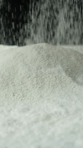 Wheat flour pouring onto a pile on a black background vertical slow motion