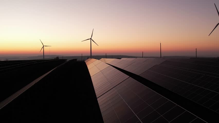  Solar panels park and wind turbines at sunset.Windmill turbines generating green energy electric.Green energy reduce carbon emissions and makes earth cleaner and more ecological.