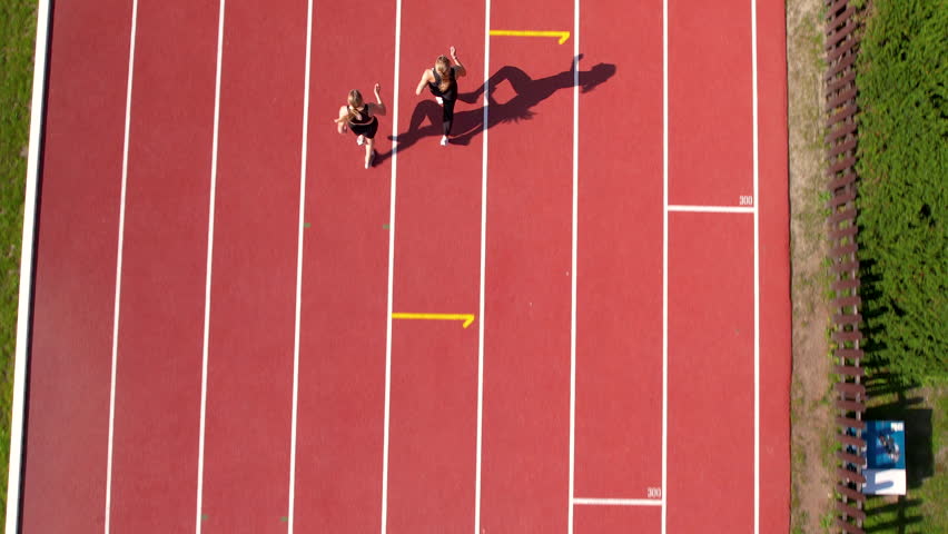 Two runners mid-stride on parallel track lanes, shadow stretching, capturing dynamic movement from above