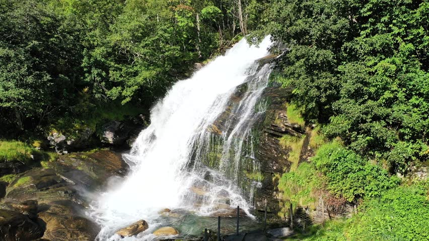 A breathtaking waterfall cascades down rocky cliffs surrounded by lush greenery in the heart of a serene forest in summer