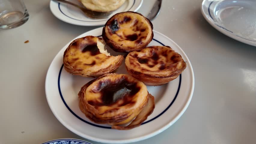 Traditional Portuguese Pastéis de Belém custard tarts on a plate with flaky crust and caramelized tops.
