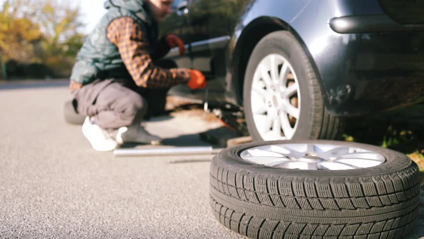 Backlit of young man change the tire of his car. Bottom shot of mechanic changing car wheel. Changing wheel on car, spare tyre by the roadside