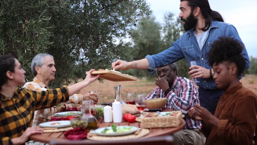 Multi ethnic group of farmers sharing a meal together outdoors in an olive grove after the olive harvest, enjoying the fruits of their labor and camaraderie