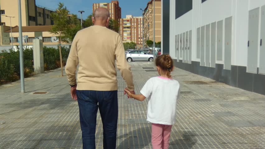 grandfather walking hand in hand with his daughter through the streets while his dog plays next to him