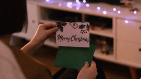 Caucasian woman sitting on a sofa in a room receives, opens and handles a Christmas card - Powered by Shutterstock - Get 15% off with code: PIKWIZARD15