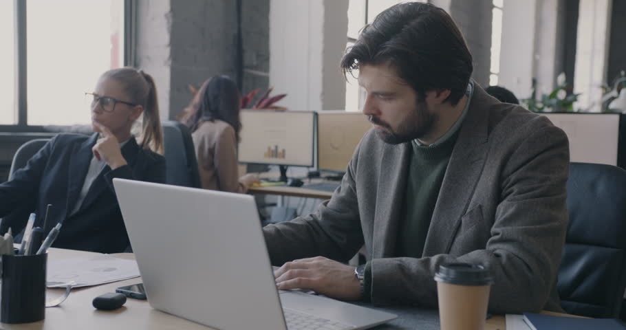 Busy employee working focused on job tasks checking time while colleagues leaving office finishing work. Overtime activity and career concept.