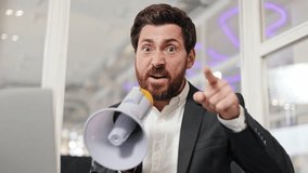 Angry businessman yells into a megaphone and points his finger at camera. Man is sitting at desk in office environment. Annoyed male in formal clothes speaking in megaphone and making hand gestures. . - Powered by Shutterstock - Get 15% off with code: PIKWIZARD15
