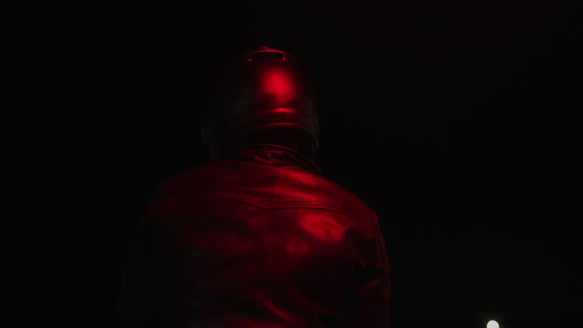 Man in black leather jacket and black helmet sits on his motorcycle and looks back. Back view. Slow motion. Extreme sport concept. Riding motorcycle requires stamina and good health