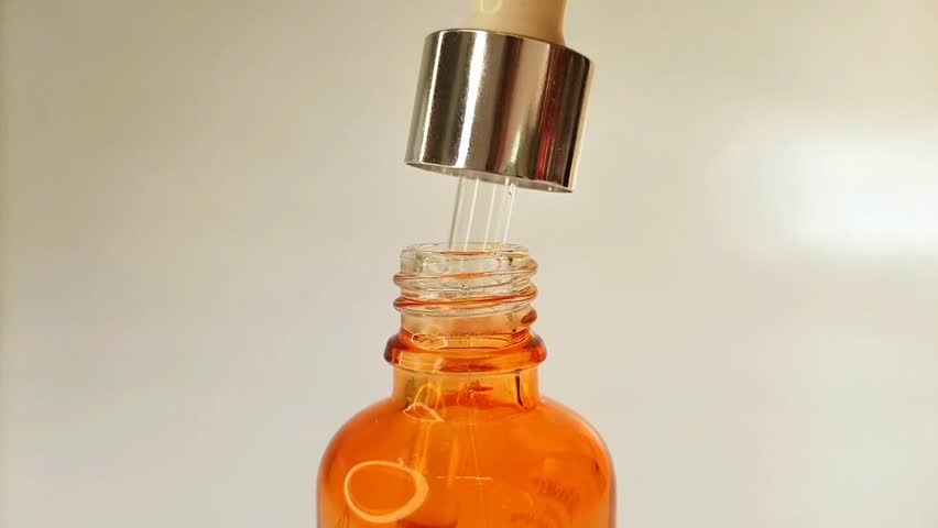 Taking out bottle pipette dropper and dripping lightweight liquid yellow-orange vitamin c or retinol serum on white background.
