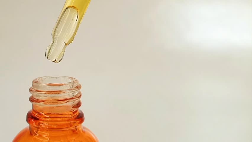 Taking out bottle pipette dropper and dripping sticky liquid yellow-orange vitamin c or retinol serum on white background, left side of the frame.