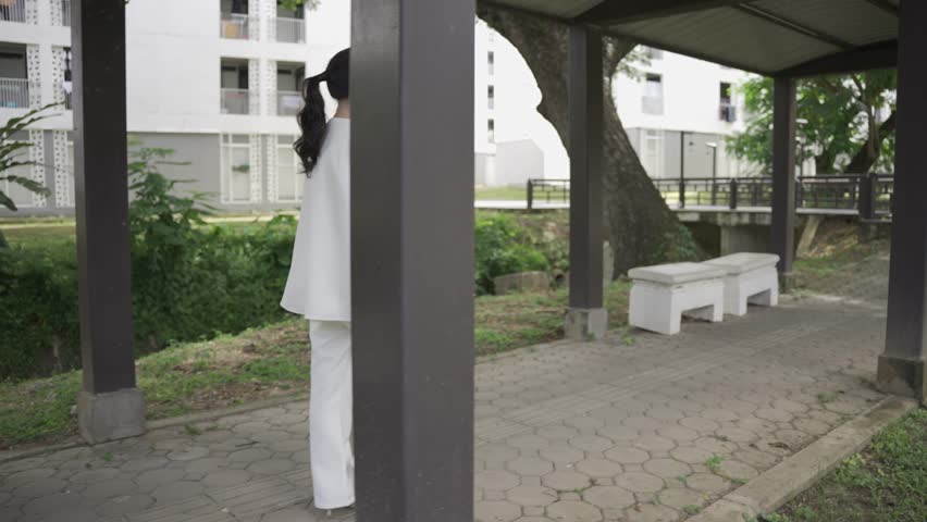 Asian businesswoman holding a tablet in a white suit is confident and independent in casual clothes. Smiling and walking down a city street during the daytime - slow motion