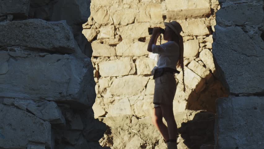 A woman looks through binoculars in the rays of a bright sun in blur. Side view