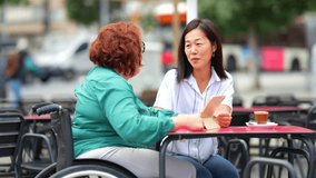Woman with disability and multi-ethnic friend talking using digital tablet in a sidewalk outdoors cafeteria - Powered by Shutterstock - Get 15% off with code: PIKWIZARD15