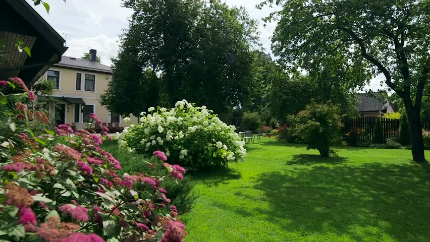 A Very Beautiful Backyard of a House with a Well-Kept Lawn, Lush Shrubs. A well-kept inner yard of the house creates a pleasant feeling for both the owners of the house and the guests.