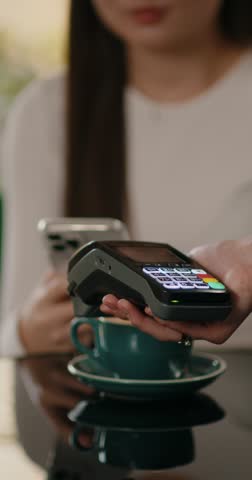 Young woman using smartphone with NFC technology to provide contactless fast payment on bank terminal. Customer paying for order with e-money in the restaurant.