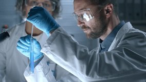 Male scientist in protective eyewear and gloves dripping blue liquid into test tube with pipette, examining chemical reaction and discussing it with female colleague in laboratory - Powered by Shutterstock - Get 15% off with code: PIKWIZARD15