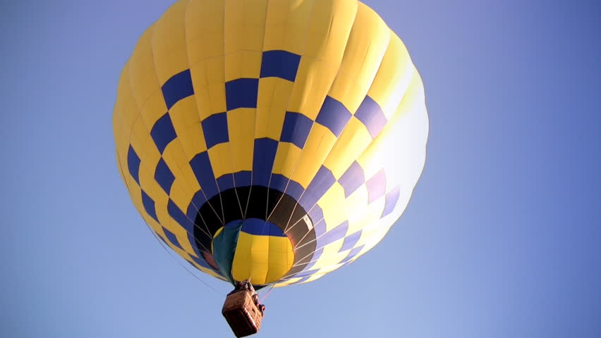 Yellow-blue Hot Air Balloon slowly rises into the blue cloudless sky. In the