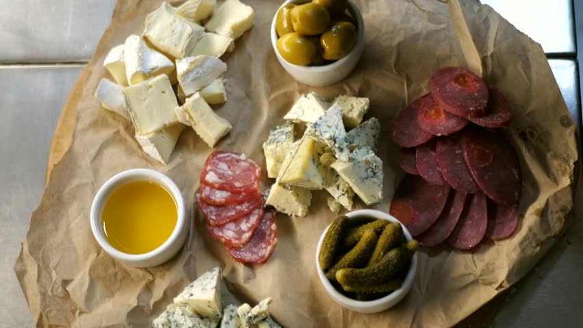 Chef decorating a meat and cheese platter. Appetizer board with assorted cheeses, salami, ham, olives and antipasto with nuts.