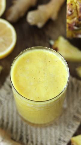 Hand is mixing and decorating yellow pineapple ginger lemon smoothie with fresh mint. Vertical video. Healthy homemade blended drink.