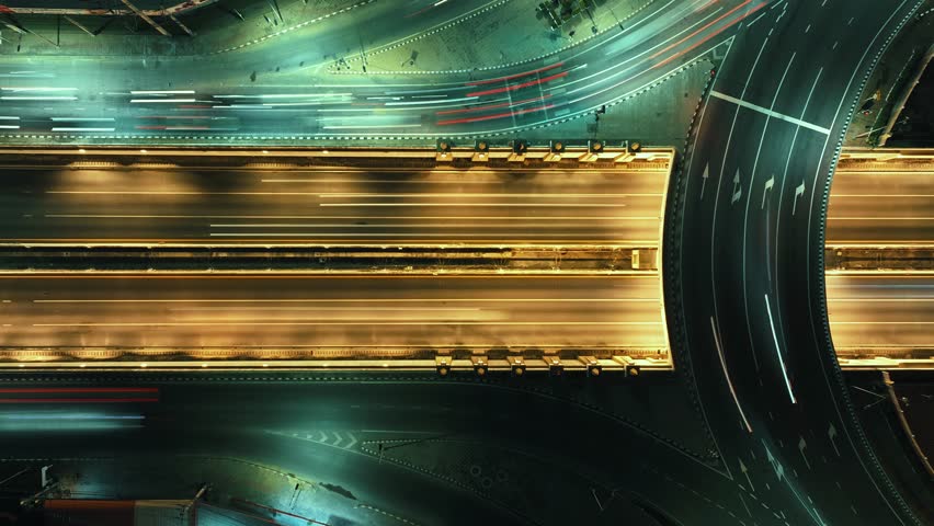 Time-lapse of car traffic transportation on road at junction intersection, 4K. Aerial view of road interchange or highway intersection with busy urban traffic speeding on the road at night. expressway