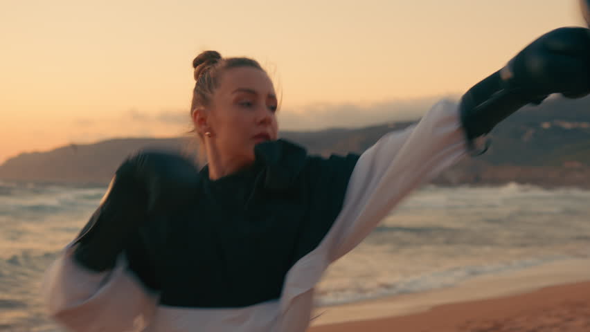 Sporty female fighters practicing boxing at beach during sunset. Determined strong young women boxers are exercising in nature. 