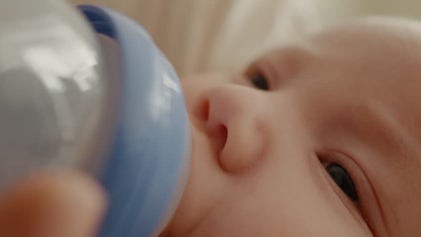 Close up of a newborn child eating from a bottle lying on bed. Mother feeds the baby using powdered milk.