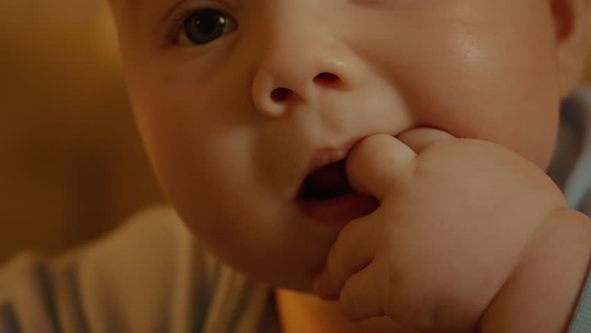 Small child sucks his fingers on his hand with itchy gums. Baby teeth are teething, gums hurt, child first year of life.