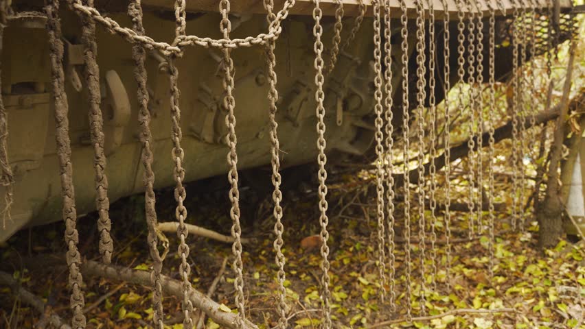 Detailed view of a military tank’s tracks and wheels, partially obscured by dirt, with fallen leaves and twigs scattered around the base.