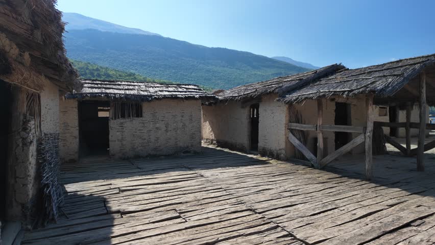 Wooden walkway leads between reconstructed pile dwellings at the Bay of bones archeological museum, situated on lake Ohrid in north Macedonia, showcasing a prehistoric settlement