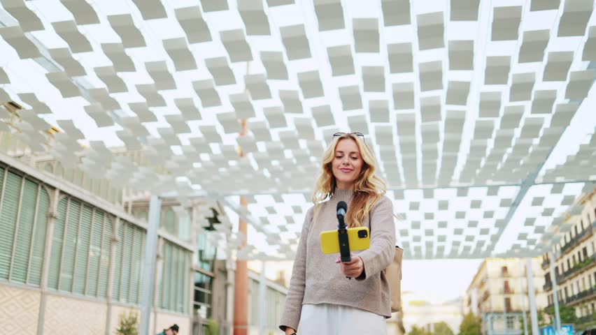 Enthusiastic travel influencer creating engaging video content for her followers while exploring a vibrant city. Influencer capturing engaging content beneath a canopy in a vibrant city