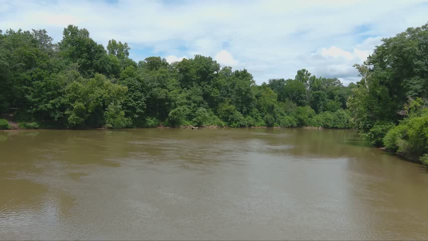 gorgeous aerial footage of the silky brown waters of the Chattahoochee river surrounded by vast miles of lush green trees and plants with powerful clouds at McIntosh Reserve Park in Whitesburg Georgia