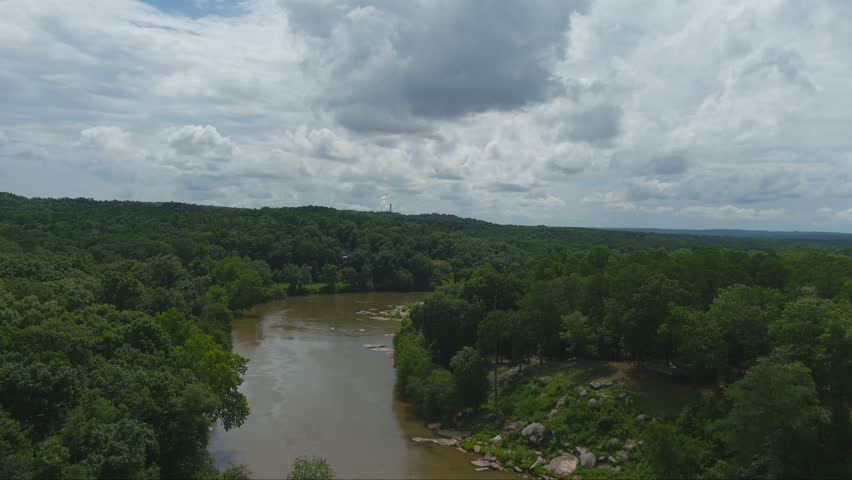 gorgeous aerial footage of the silky brown waters of the Chattahoochee river surrounded by vast miles of lush green trees and plants with powerful clouds at McIntosh Reserve Park in Whitesburg Georgia