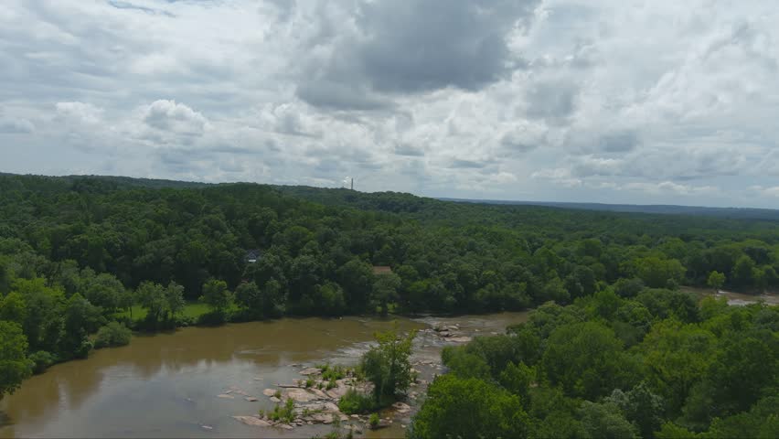 gorgeous aerial footage of the silky brown waters of the Chattahoochee river surrounded by vast miles of lush green trees and plants with powerful clouds at McIntosh Reserve Park in Whitesburg Georgia