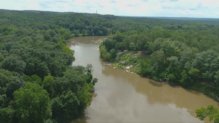 gorgeous aerial footage of the silky brown waters of the Chattahoochee river surrounded by vast miles of lush green trees and plants with powerful clouds at McIntosh Reserve Park in Whitesburg Georgia