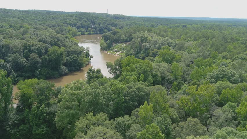 gorgeous aerial footage of the silky brown waters of the Chattahoochee river surrounded by vast miles of lush green trees and plants with powerful clouds at McIntosh Reserve Park in Whitesburg Georgia