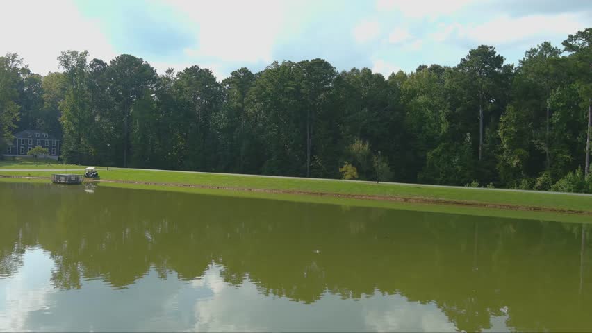 aerial footage of a silky green lake surrounded by vast miles of lush green trees with birds on the water and blue sky with clouds at Huddleston Pond Park in Peachtree City Georgia USA