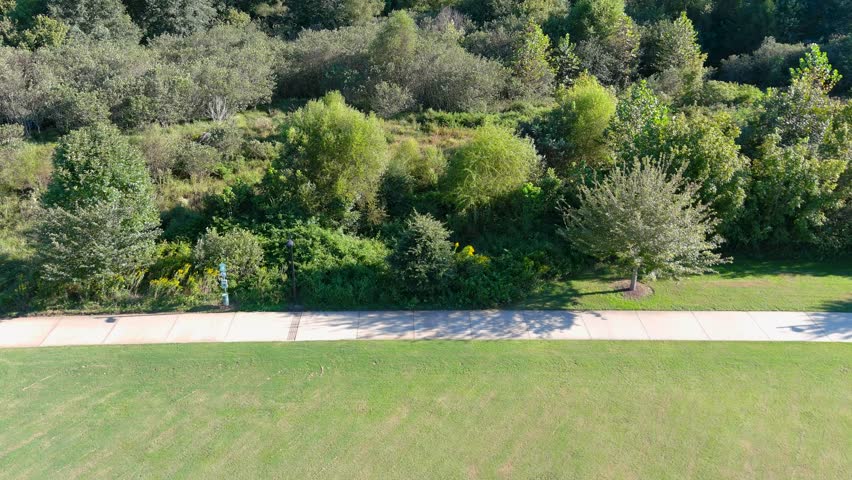 aerial footage of a gorgeous autumn landscape in the park along a long smooth winding footpath surrounded by lush green trees, grass and plants at Etowah River Park in Canton Georgia USA