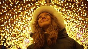 Young woman smiles while gazing up at twinkling christmas lights. Dressed in a winter coat and a cozy white furry hat, she radiates joy in the festive evening atmosphere - Powered by Shutterstock - Get 15% off with code: PIKWIZARD15