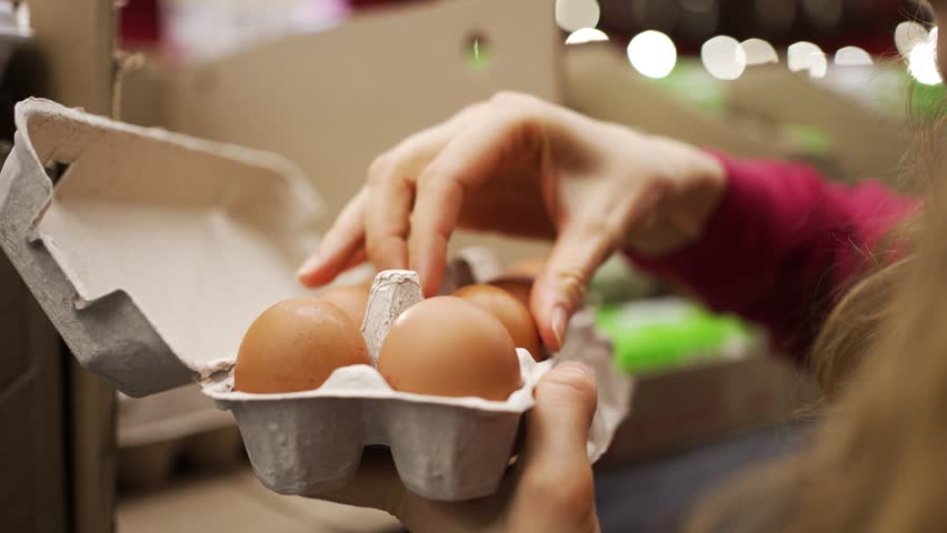  Woman chooses chicken eggs on a supermarket shelf. He opens a cardboard box and looks through each egg, discards the cracked ones.