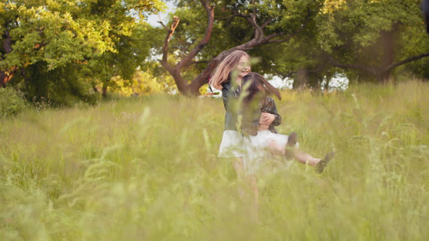 Pretty sisters in positive mood relaxing on fresh air. Caucasian sisters playing together at green garden. Two caucasian little girls in summer dress and black jacket playing together at summer garden