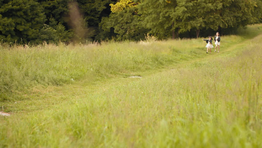 Two caucasian little girls in summer dress and black jacket playing together at summer garden. Pretty sisters in positive mood relaxing on fresh air. Two sisters run across the field
