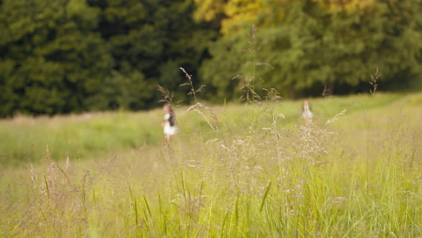 Two caucasian little girls in summer dress and black jacket playing together at summer garden. Pretty sisters in positive mood relaxing on fresh air. Two sisters run in the garden outdoors.
