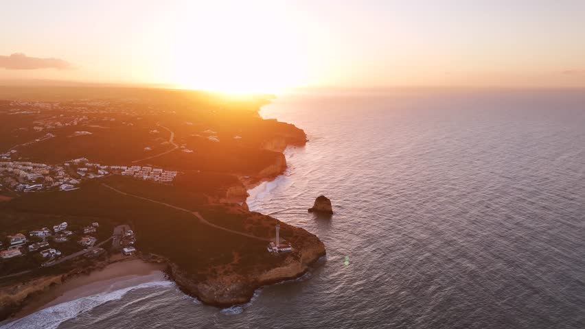 Sunrise above Algarve shoreline in Portugal. The cape with the lighthouse Farol da Ponta do Altar are in the foreground 