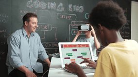Girl wear VR glass while mentor pointing at blackboard and explain engineering code. African student writing system while receive advice from teacher at table with electronic equipment. Edification - Powered by Shutterstock - Get 15% off with code: PIKWIZARD15