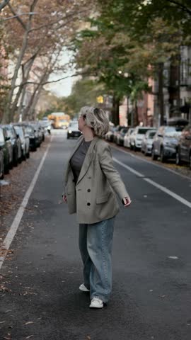 A fashionable woman is happily enjoying a leisurely walk along a picturesque street adorned with autumn colors