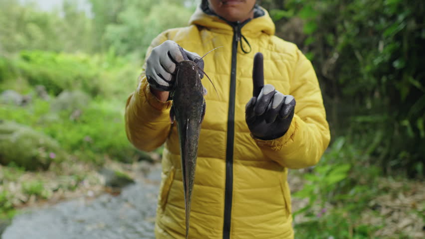 A man holds an invasive fish found in nature and rejects releasing it. Campaign against releasing invasive fish to protect natural water environments.