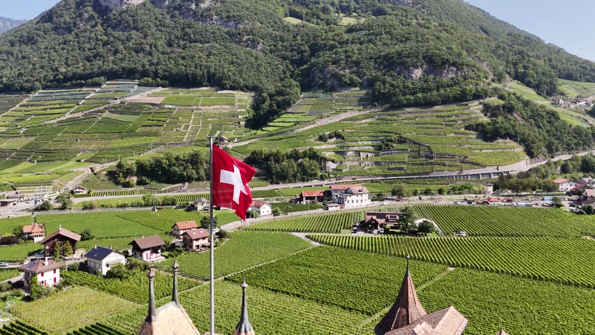 Aerial shot of waving Swiss flag with Canton of Vaud landscape, Switzerland